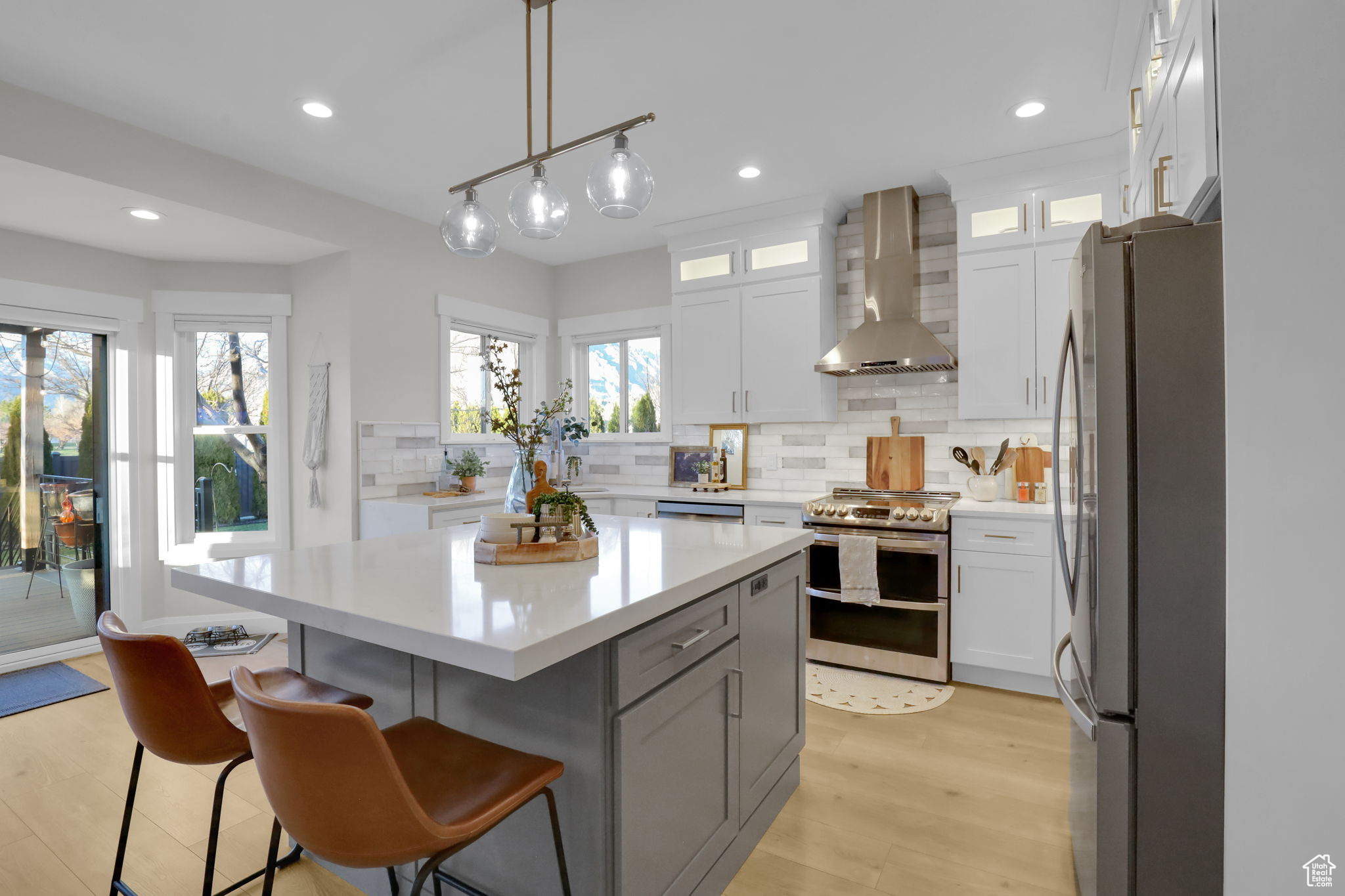 Kitchen featuring light wood-type flooring, stainless steel appliances, a breakfast bar area, wall chimney exhaust hood, and a kitchen island