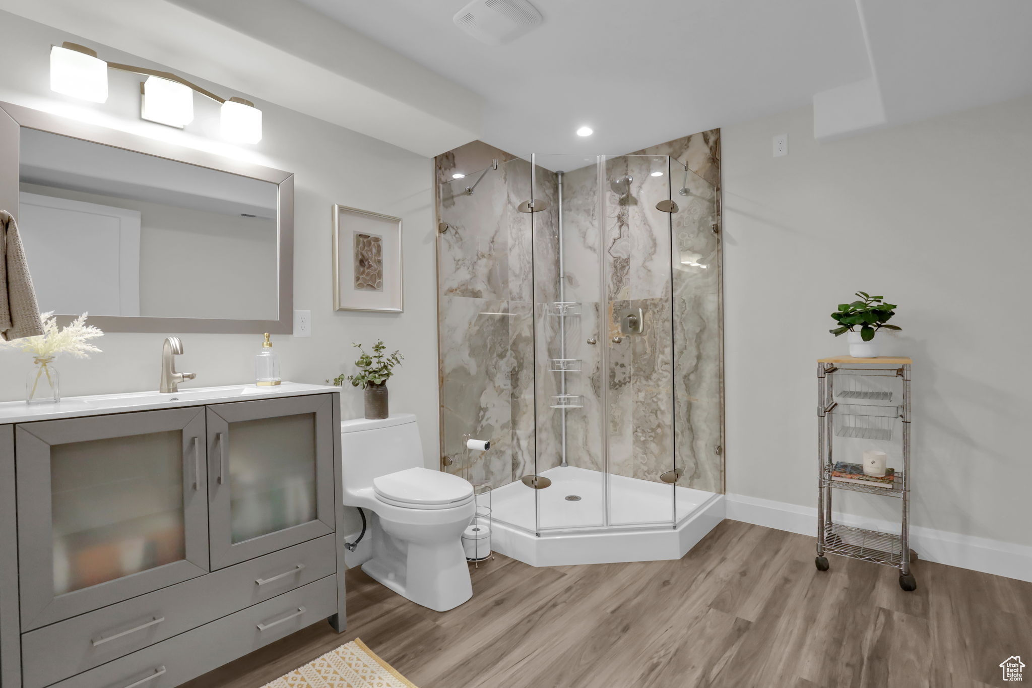 Bathroom with an enclosed shower, toilet, vanity with extensive cabinet space, and hardwood / wood-style floors