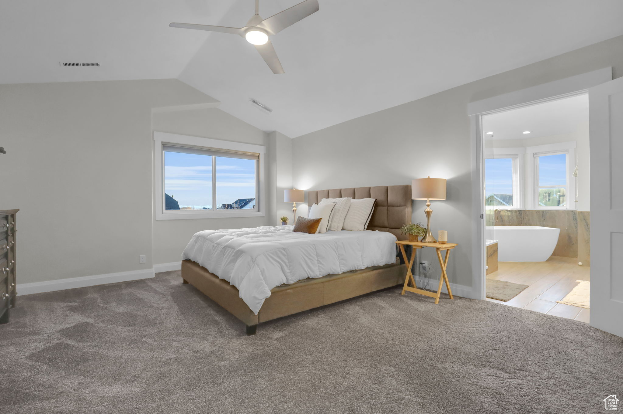 Bedroom with light colored carpet, ensuite bath, lofted ceiling, and ceiling fan