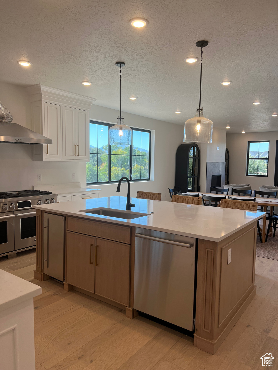 Kitchen featuring appliances with stainless steel finishes, white cabinets, hanging light fixtures, a kitchen island with sink, and light wood-type flooring