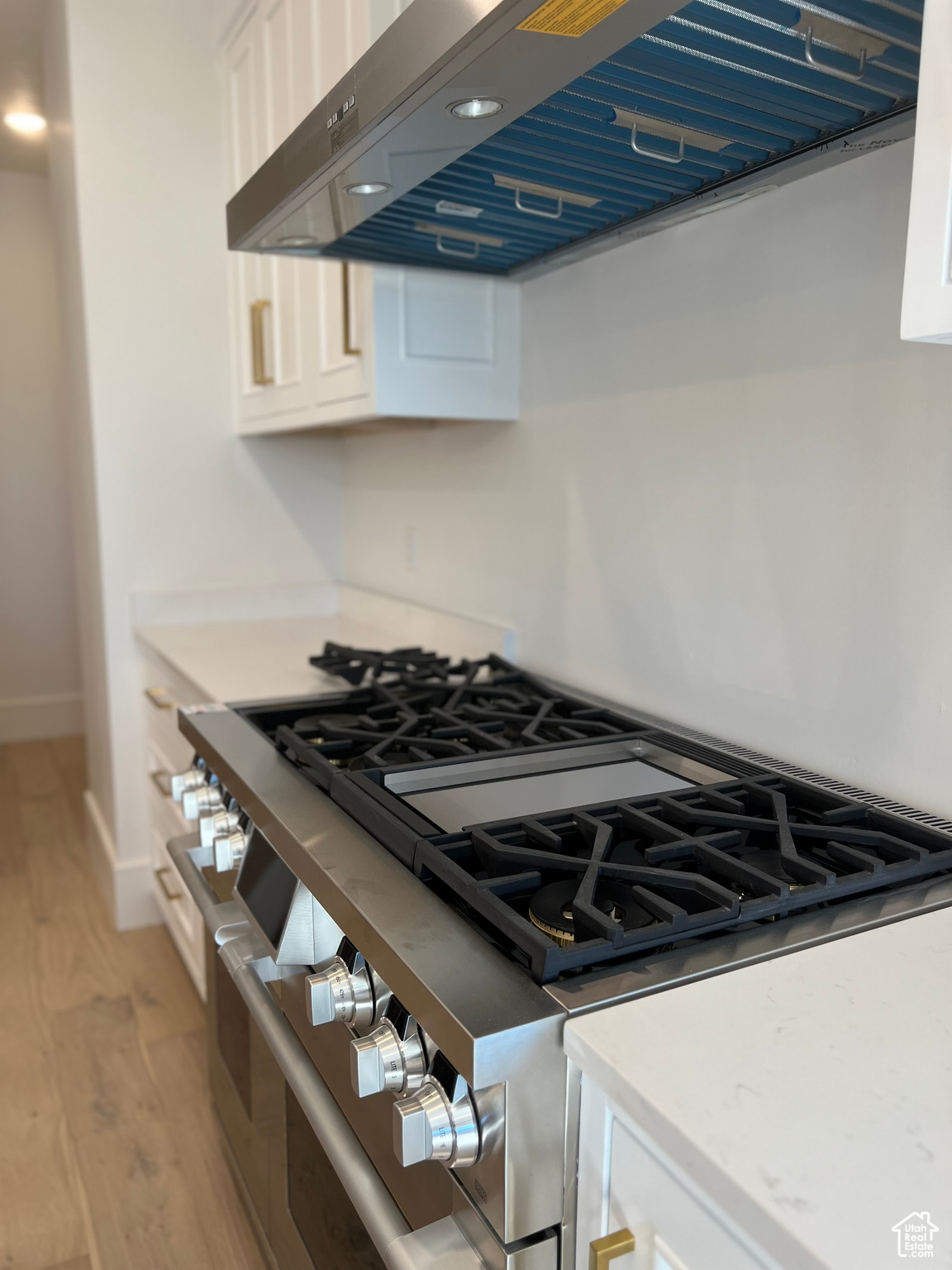 Kitchen with light hardwood / wood-style floors, double oven range, wall chimney range hood, white cabinets, and backsplash