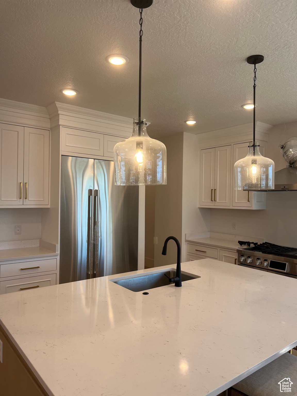 Kitchen with high quality fridge, white cabinets, pendant lighting, and sink