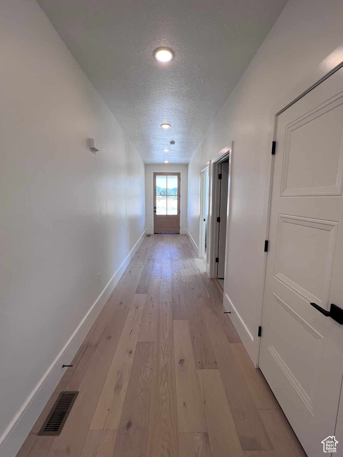 Hall featuring a textured ceiling and light hardwood / wood-style flooring