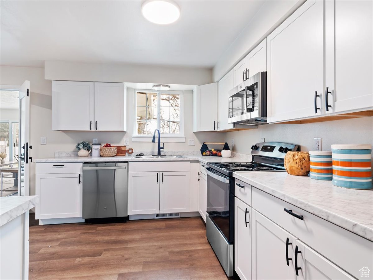 Kitchen featuring white cabinets, wood-type flooring, appliances with stainless steel finishes, and sink