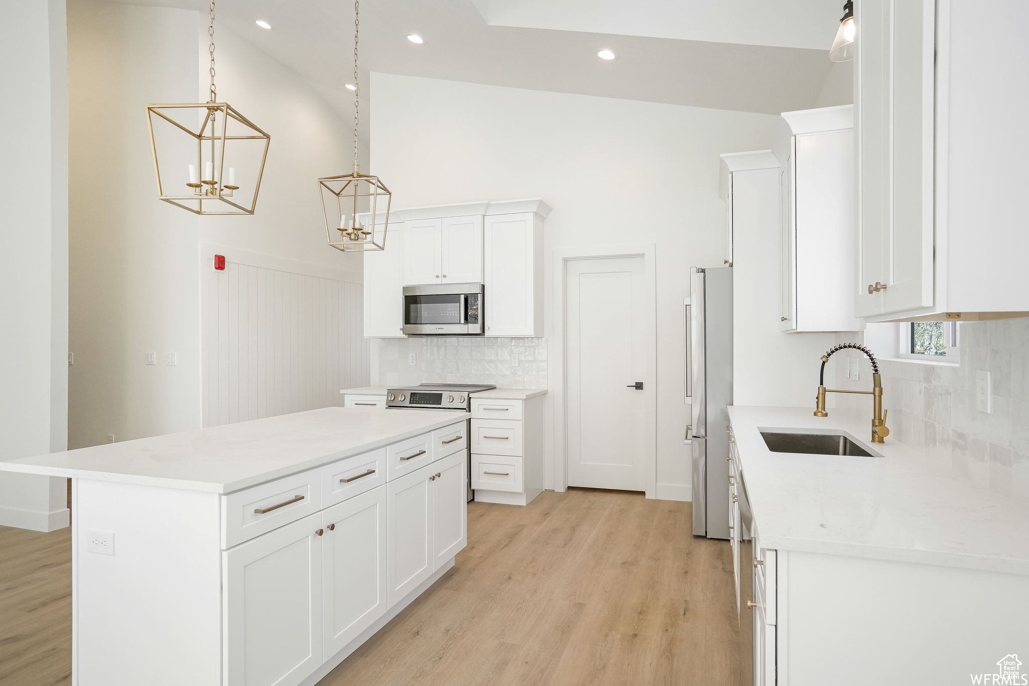 Kitchen with white cabinets, stainless steel appliances, backsplash, and light hardwood / wood-style floors