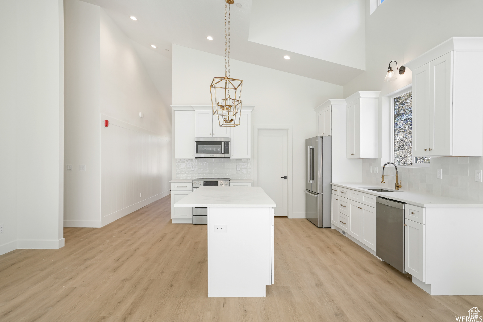 Kitchen featuring appliances with stainless steel finishes, high vaulted ceiling, light wood-type flooring, a center island, and tasteful backsplash