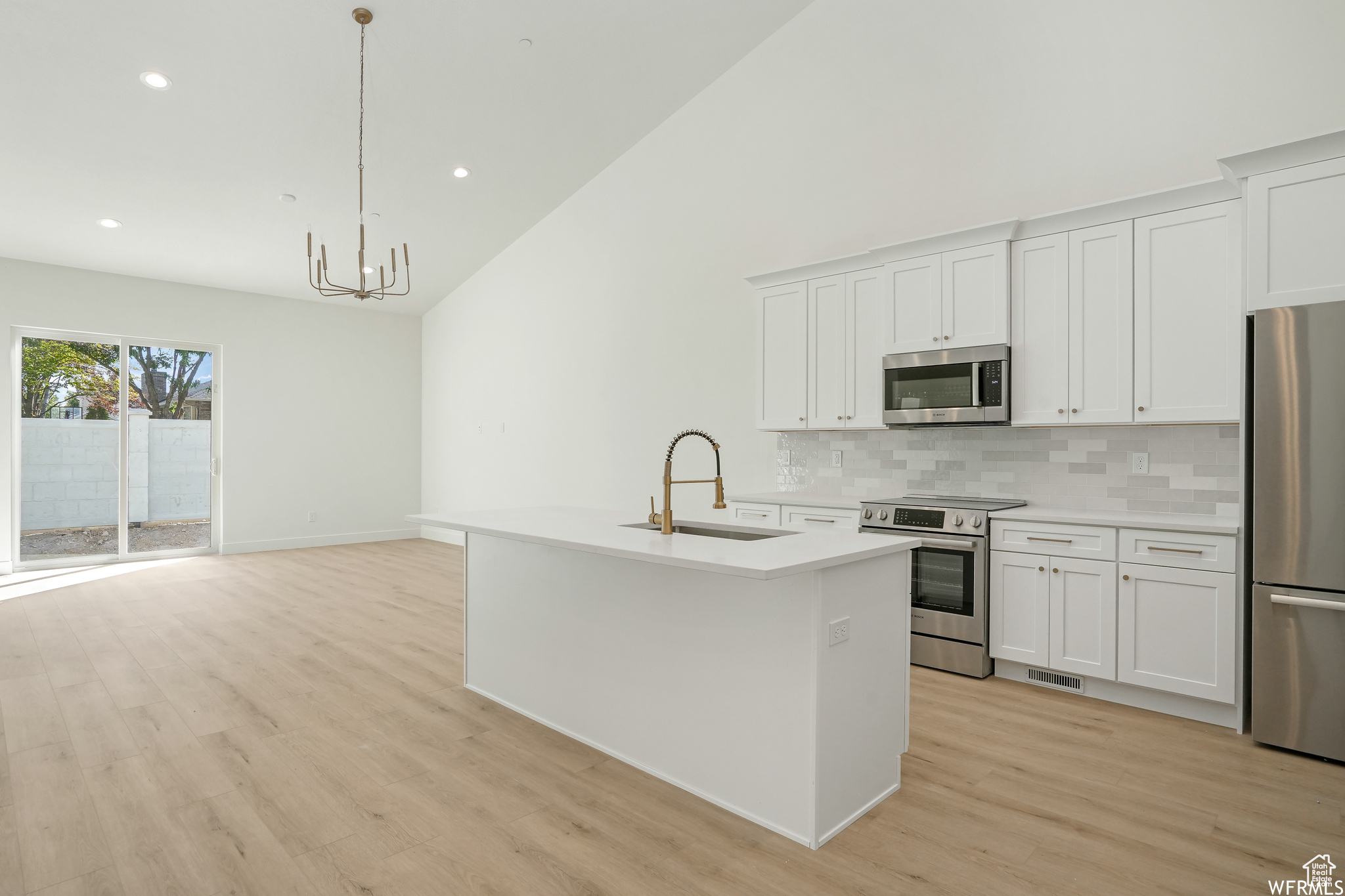 Kitchen with stainless steel appliances, decorative light fixtures, a notable chandelier, white cabinetry, and light hardwood / wood-style flooring