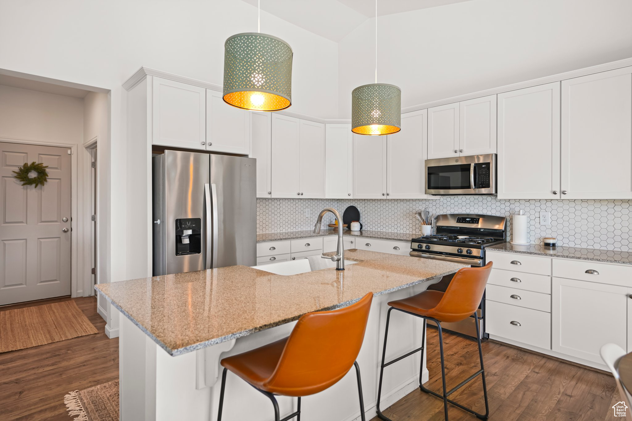 Kitchen featuring pendant lighting, backsplash, dark hardwood / wood-style floors, appliances with stainless steel finishes, and a kitchen island with sink