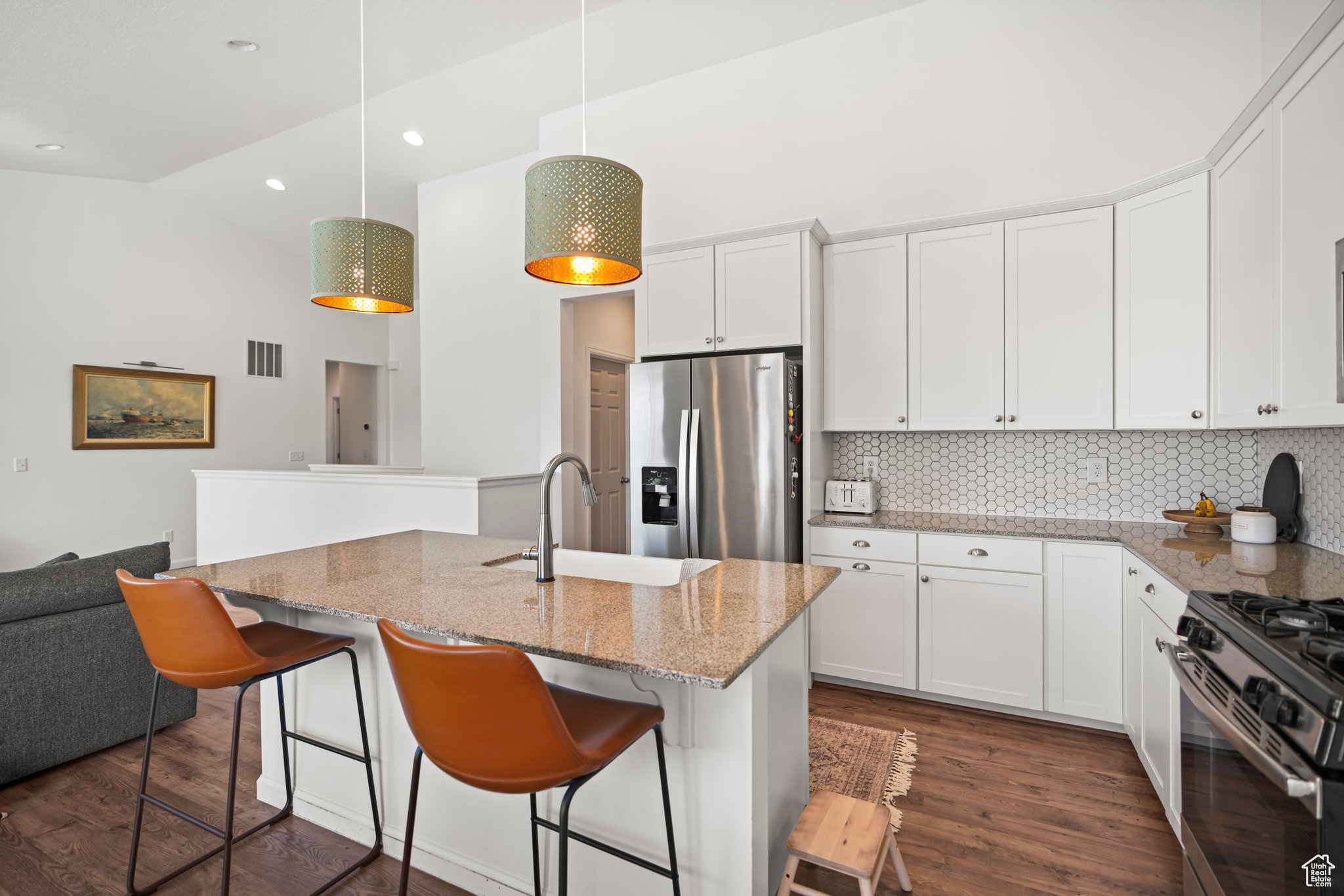 Kitchen featuring white cabinets, tasteful backsplash, appliances with stainless steel finishes, light stone countertops, and hanging light fixtures
