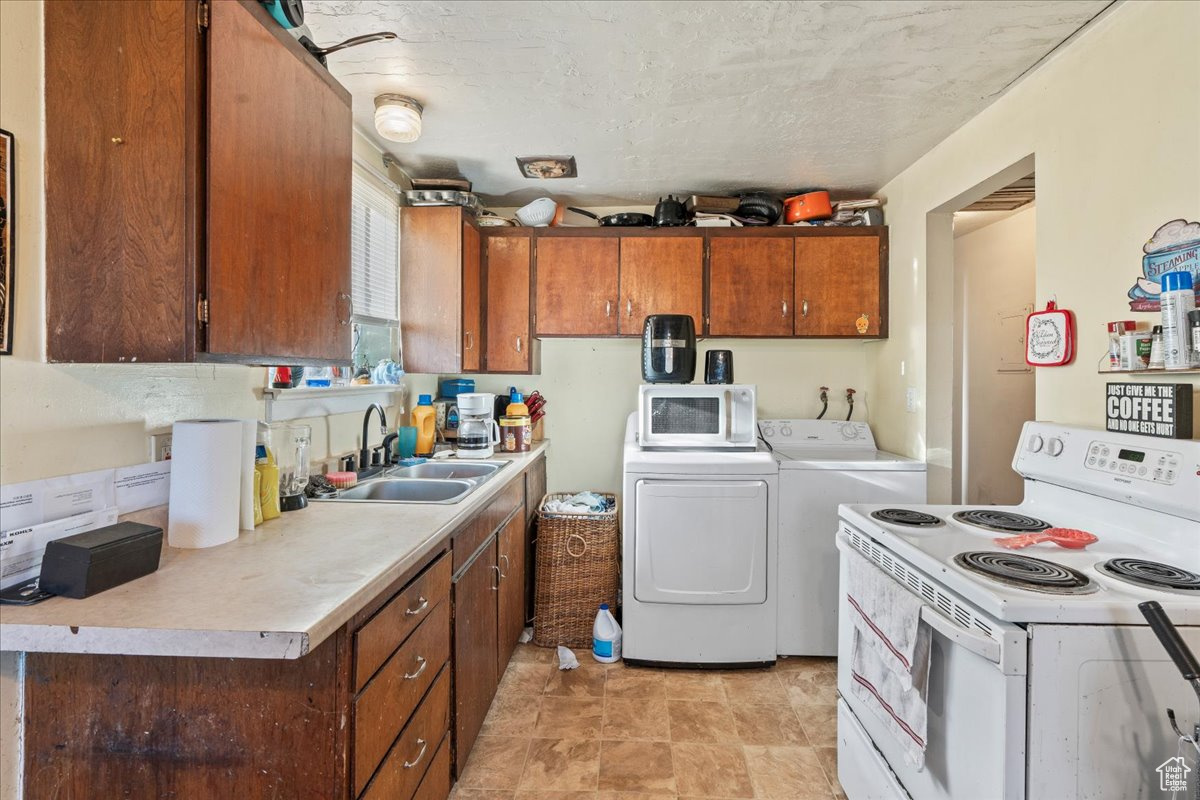 Kitchen featuring washer and dryer, light tile flooring, white appliances, and sink