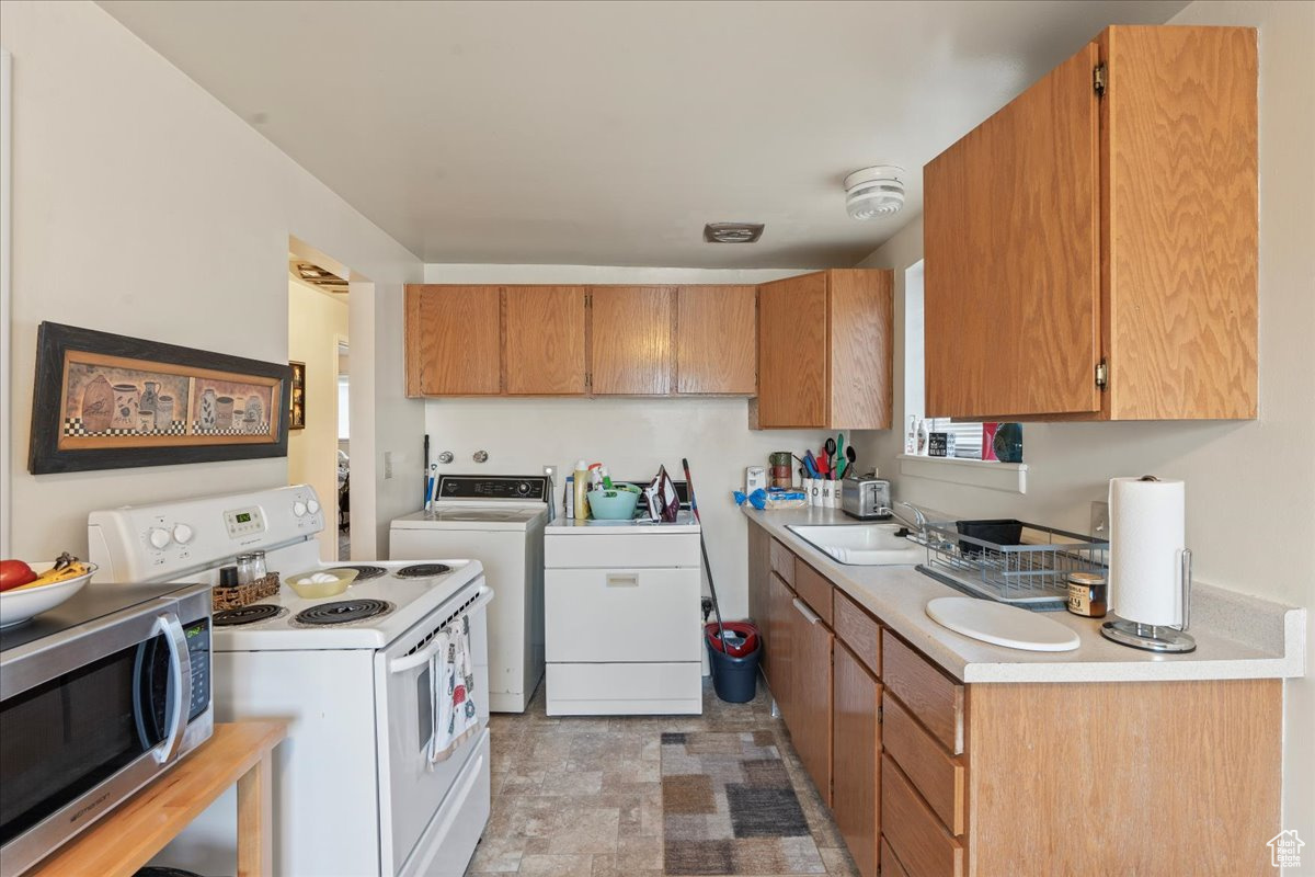 Kitchen with washing machine and clothes dryer, white range with electric cooktop, sink, and light tile floors