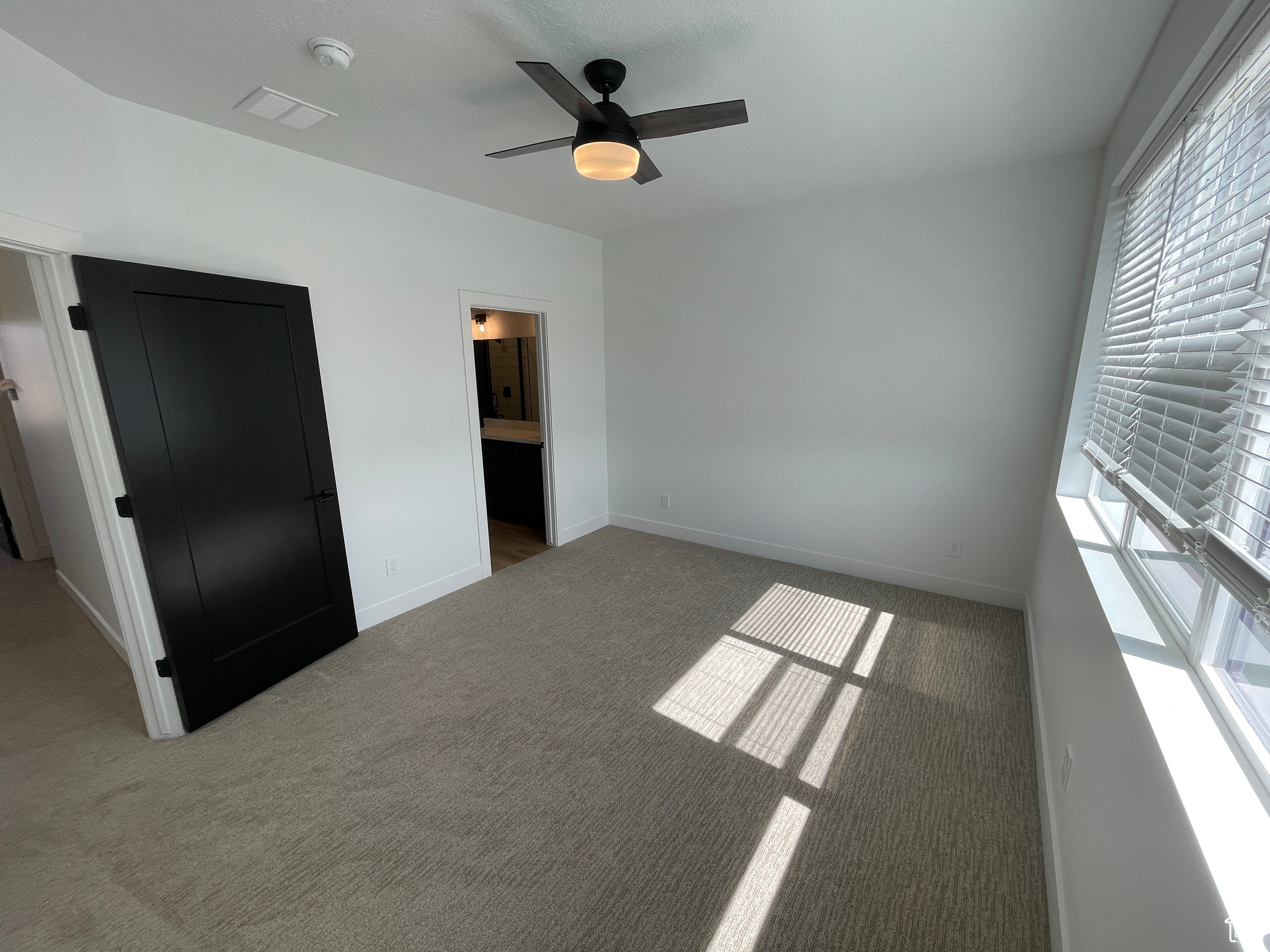 Unfurnished bedroom with light carpet, ensuite bathroom, and ceiling fan