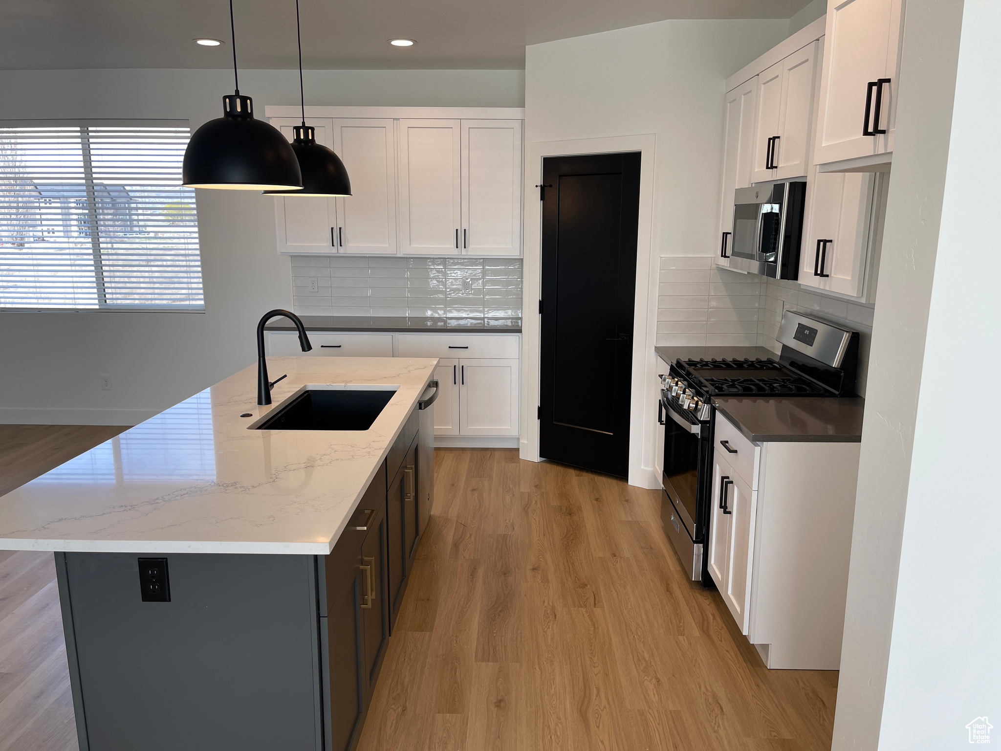 Kitchen featuring sink, white cabinets, a center island with sink, stainless steel appliances, and decorative light fixtures
