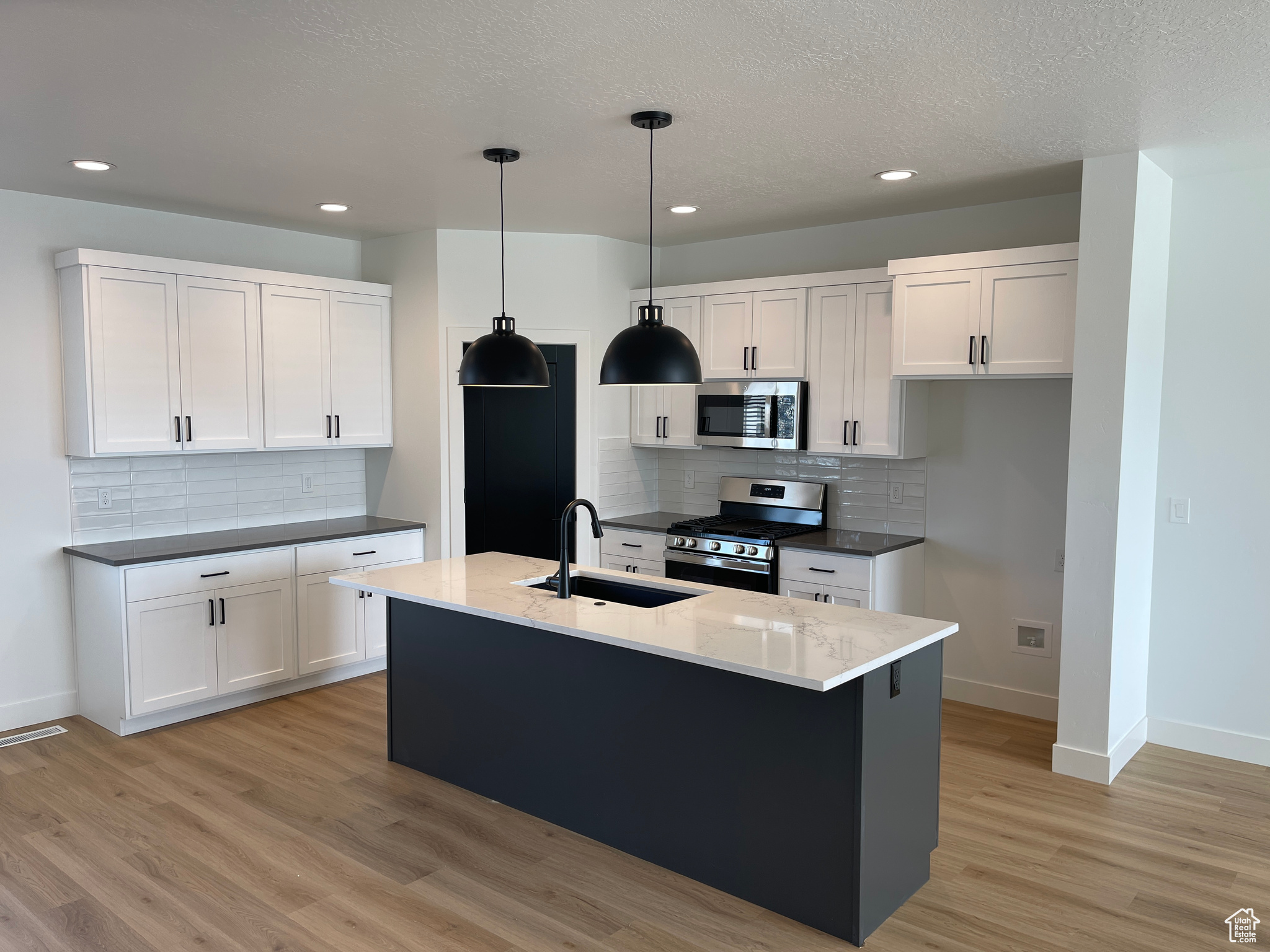 Kitchen featuring a kitchen island with sink, pendant lighting, white cabinets, light hardwood / wood-style floors, and stainless steel appliances