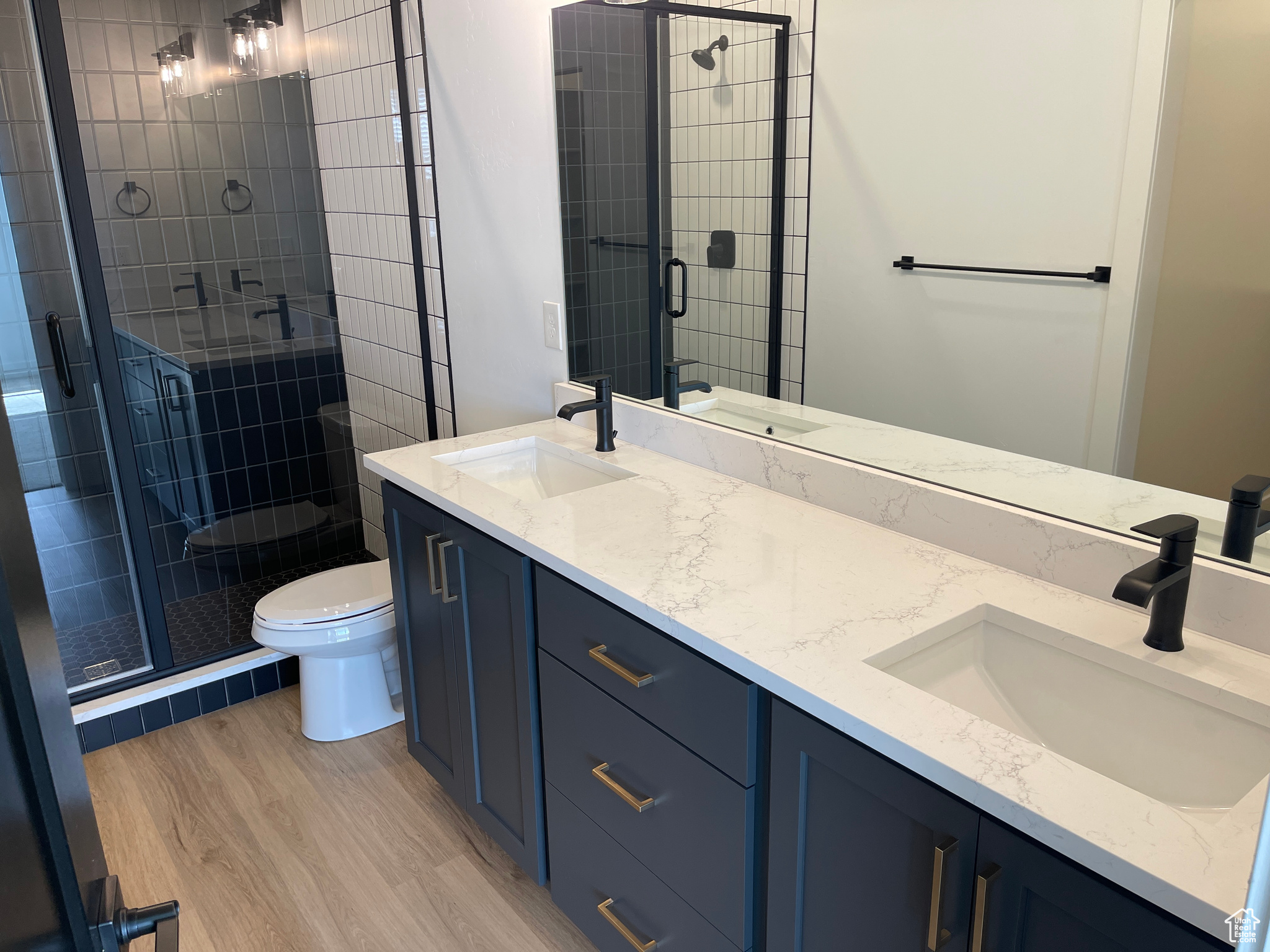 Bathroom featuring a shower with door, toilet, double sink vanity, and hardwood / wood-style flooring