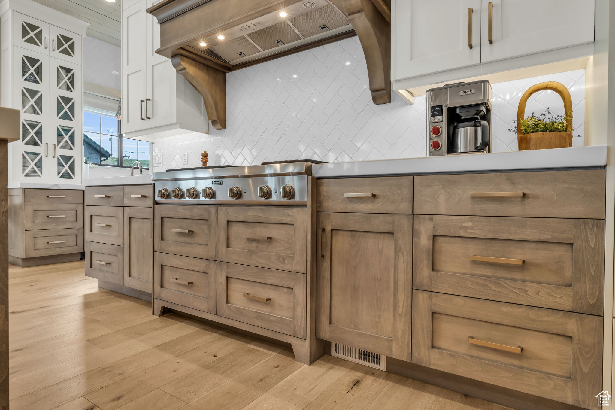 Kitchen with tasteful backsplash, premium range hood, white cabinetry, and light hardwood / wood-style flooring