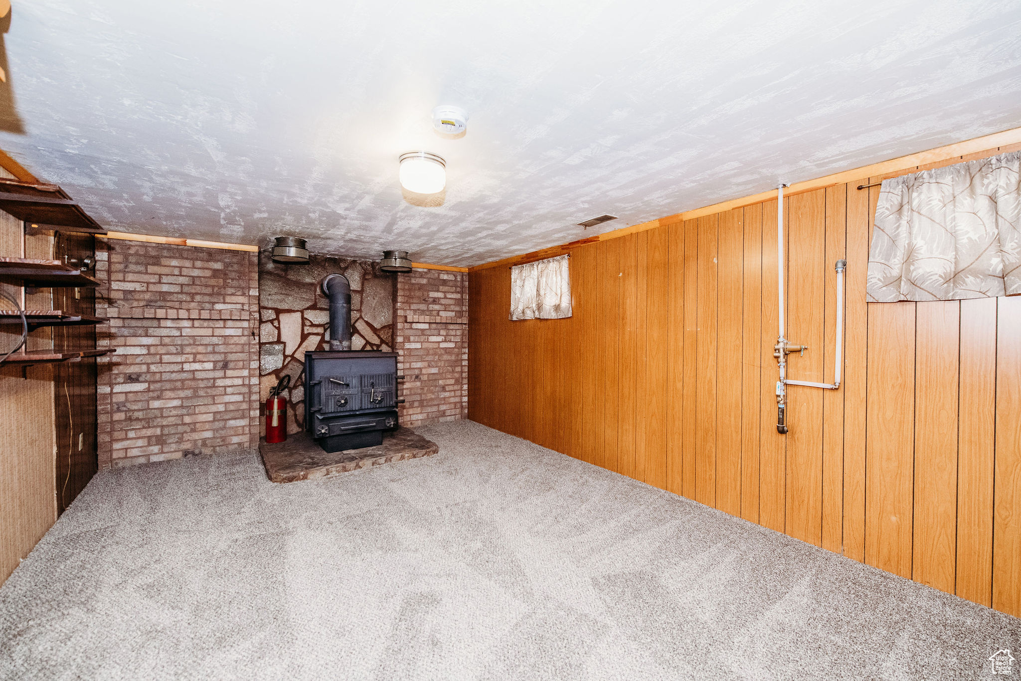 Basement with carpet floors, wood walls, and a wood stove