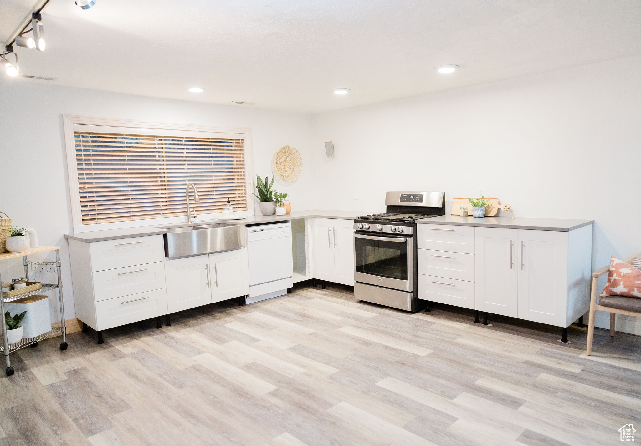 Basement kitchen featuring sink, stainless steel gas range oven, dishwasher, white cabinetry, and light wood-type flooring
