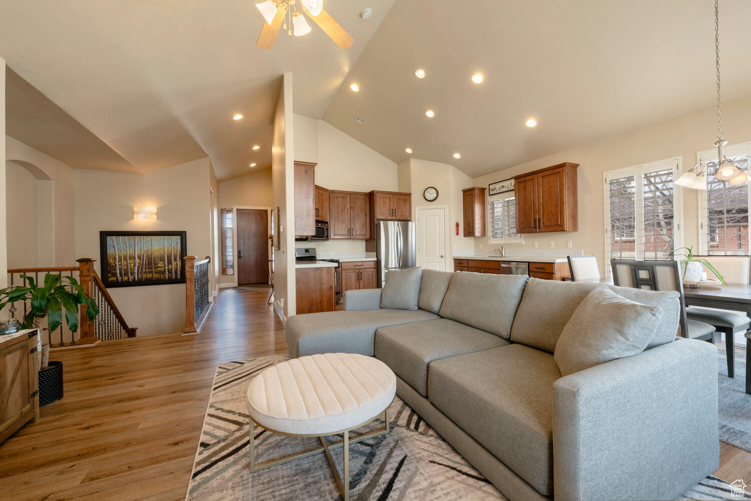 Living room with high vaulted ceiling, light hardwood / wood-style floors, and ceiling fan with notable chandelier