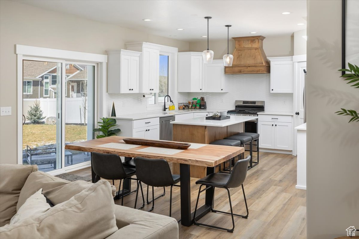 Kitchen featuring a kitchen island, appliances with stainless steel finishes, white cabinets, premium range hood, and light wood-type flooring