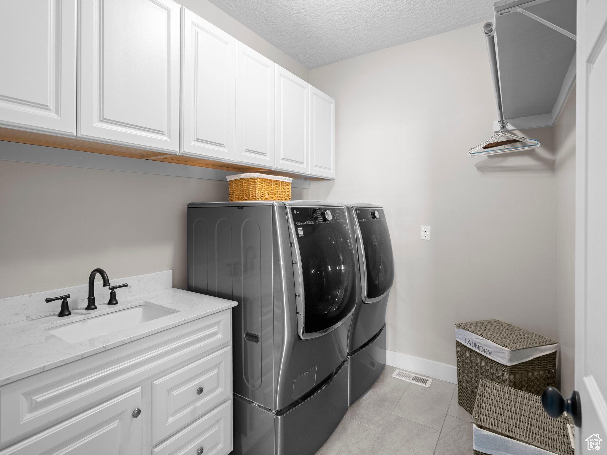 Laundry area featuring washing machine and dryer, cabinets, sink, light tile floors, and a textured ceiling