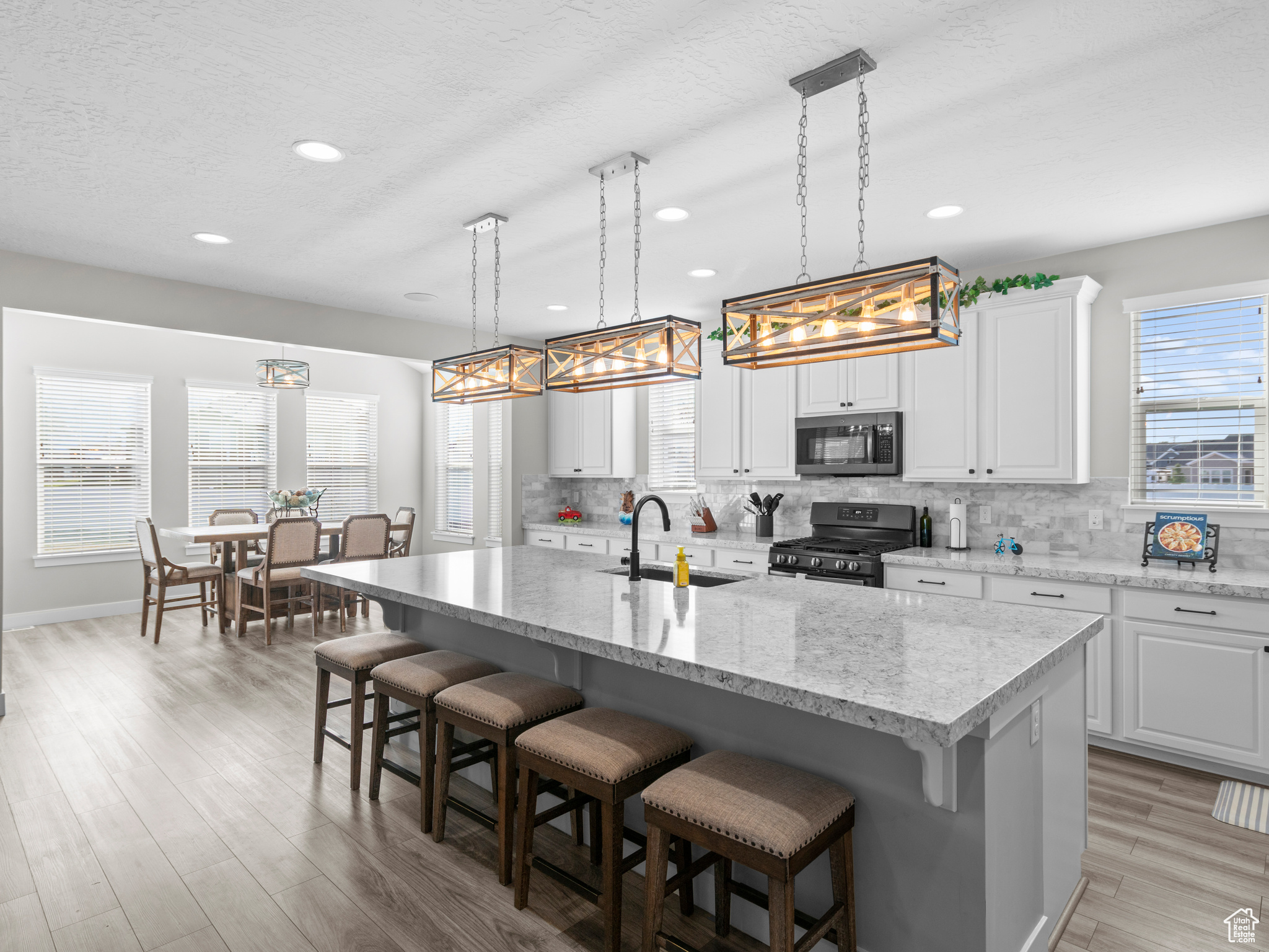 Kitchen featuring an island with sink, decorative light fixtures, gas range oven, white cabinets, and sink