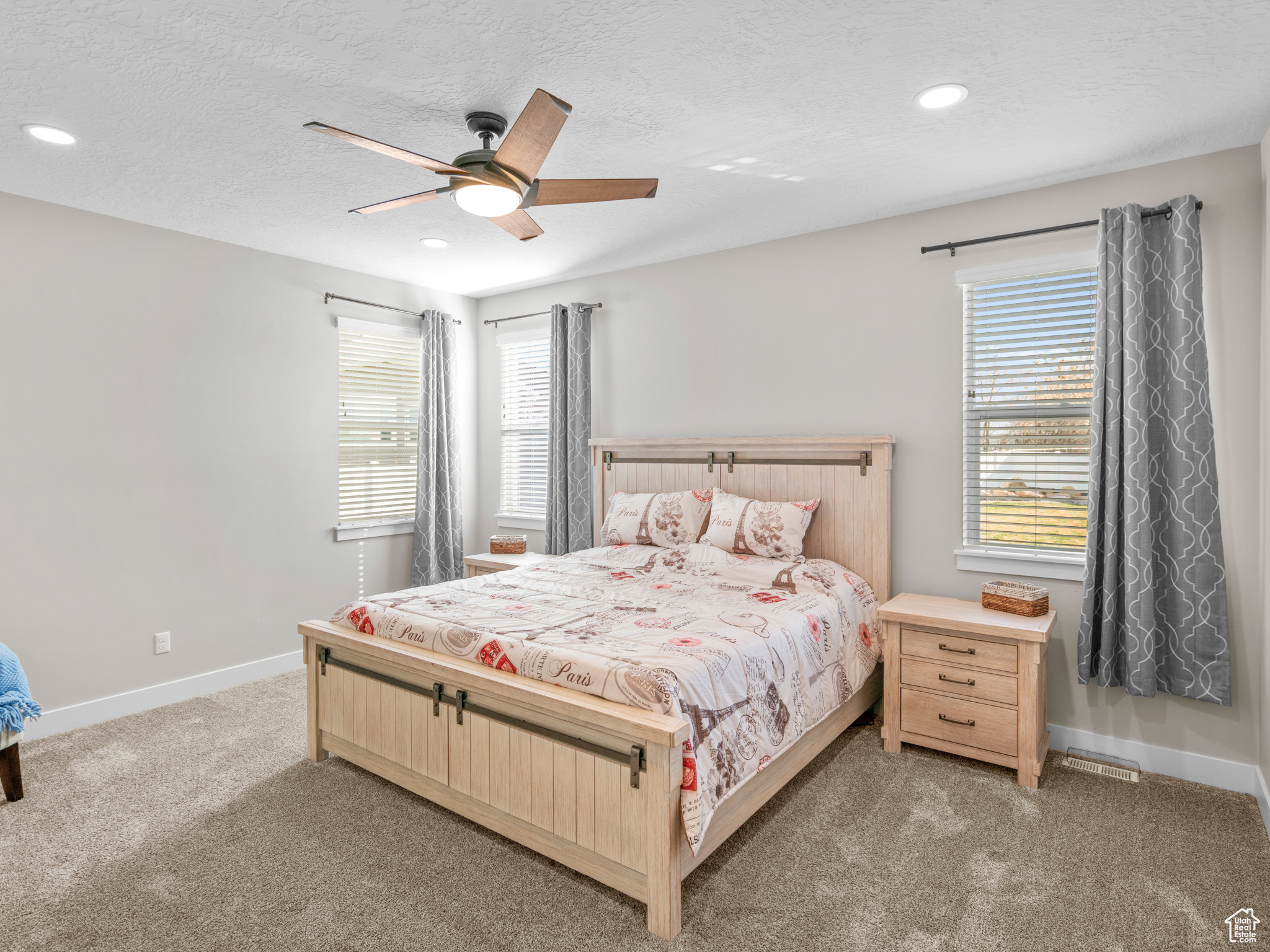 Carpeted bedroom with ceiling fan, a textured ceiling, and multiple windows