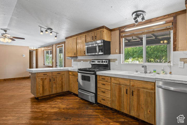 Kitchen with appliances with stainless steel finishes, dark hardwood / wood-style flooring, a healthy amount of sunlight, and ceiling fan