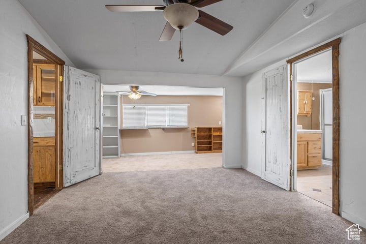 Carpeted empty room with lofted ceiling and ceiling fan