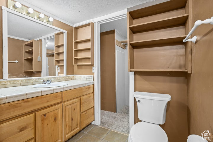 Bathroom with a textured ceiling, tile patterned floors, toilet, vanity, and ornamental molding