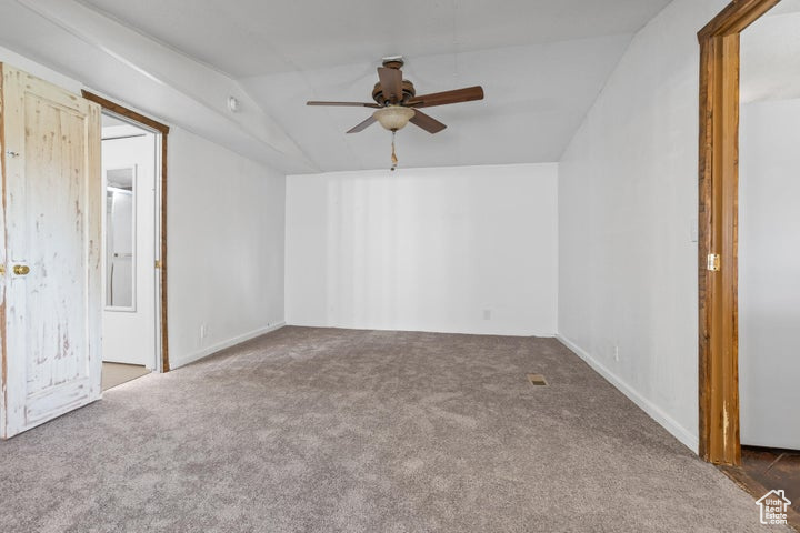 Carpeted empty room with ceiling fan and vaulted ceiling