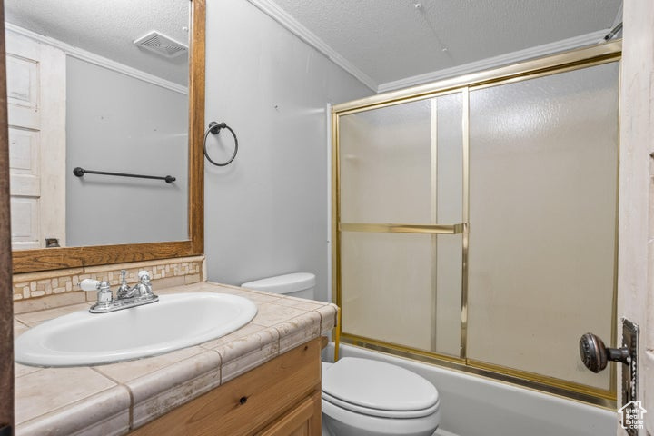 Full bathroom featuring vanity, crown molding, bath / shower combo with glass door, toilet, and a textured ceiling