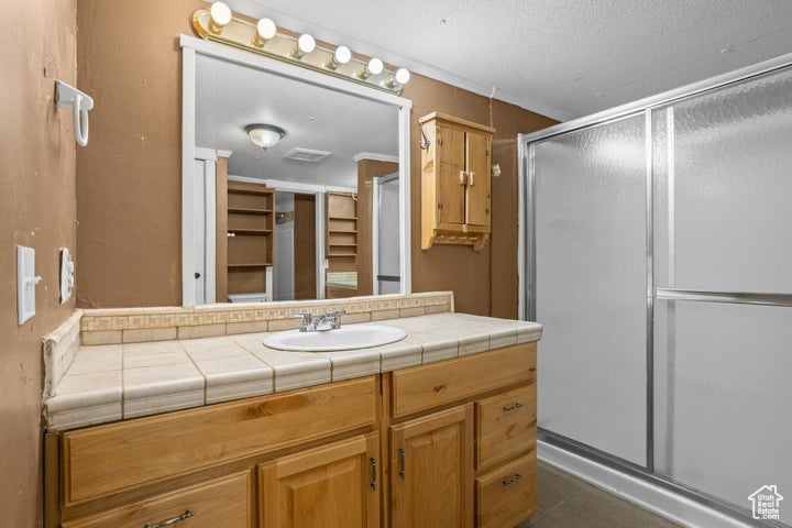 Bathroom with tile patterned floors, a shower with door, vanity, and a textured ceiling