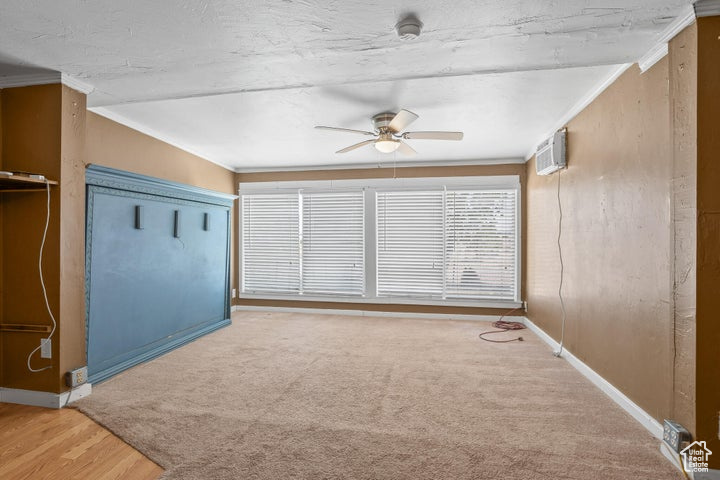 Unfurnished room featuring an AC wall unit, carpet, ceiling fan, and ornamental molding