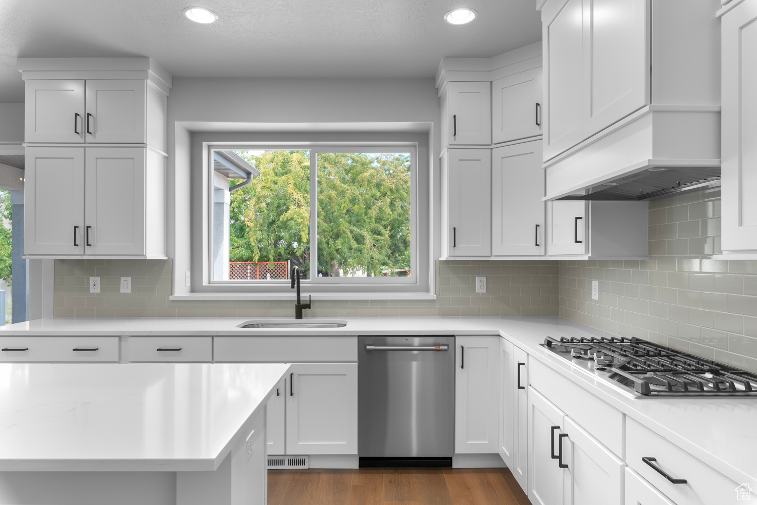 Kitchen with appliances with stainless steel finishes, premium range hood, tasteful backsplash, sink, and hardwood / wood-style flooring