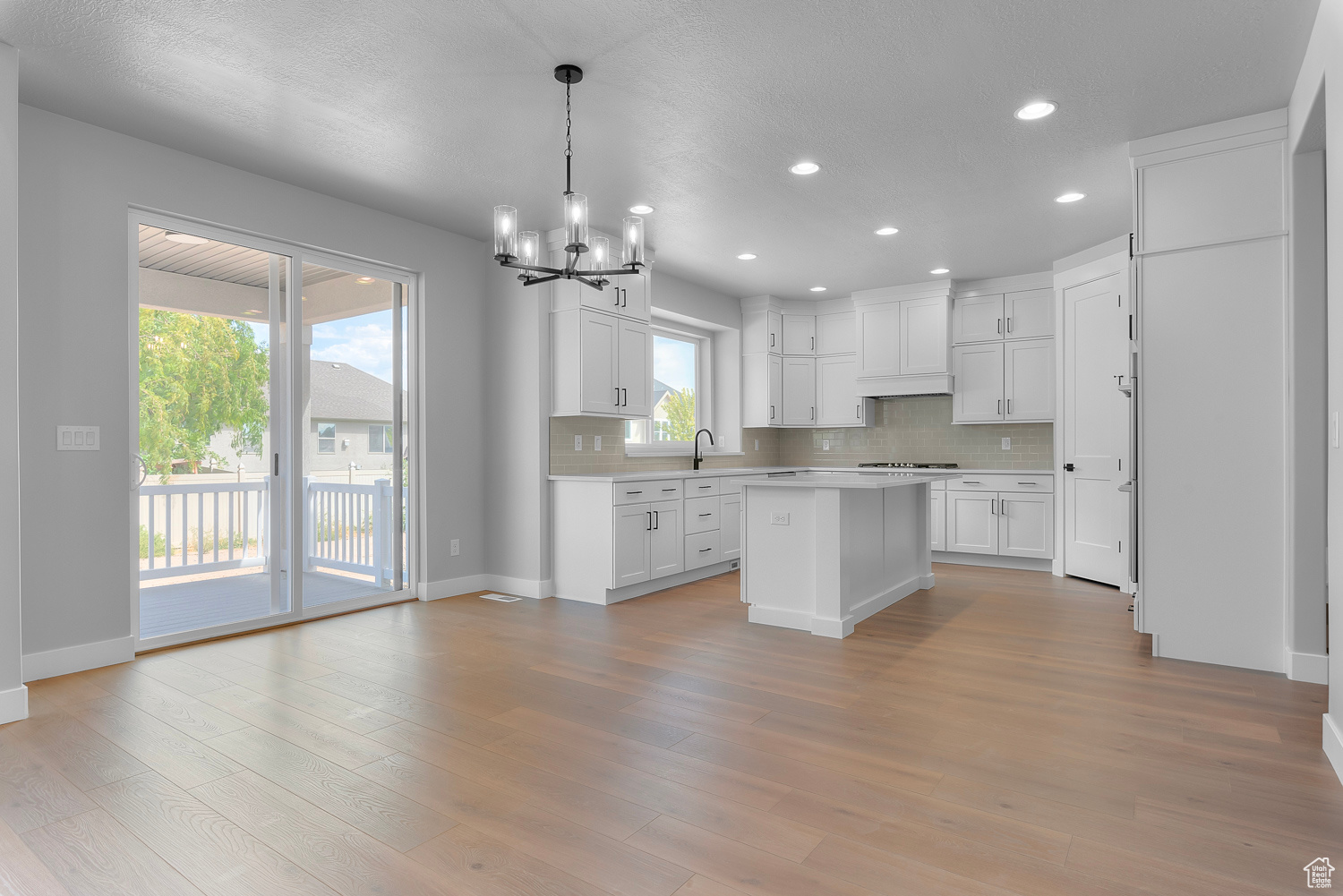 Kitchen with backsplash, light hardwood / wood-style flooring, decorative light fixtures, white cabinets, and a center island