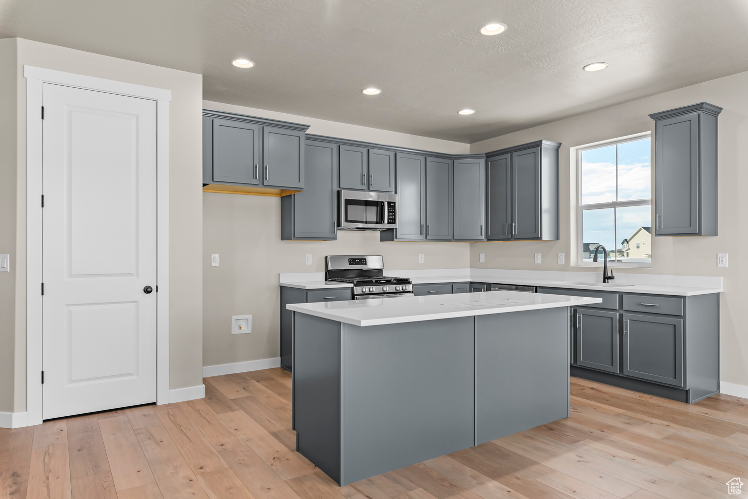 Kitchen with appliances with stainless steel finishes, gray cabinetry, sink, light hardwood / wood-style floors, and a kitchen island