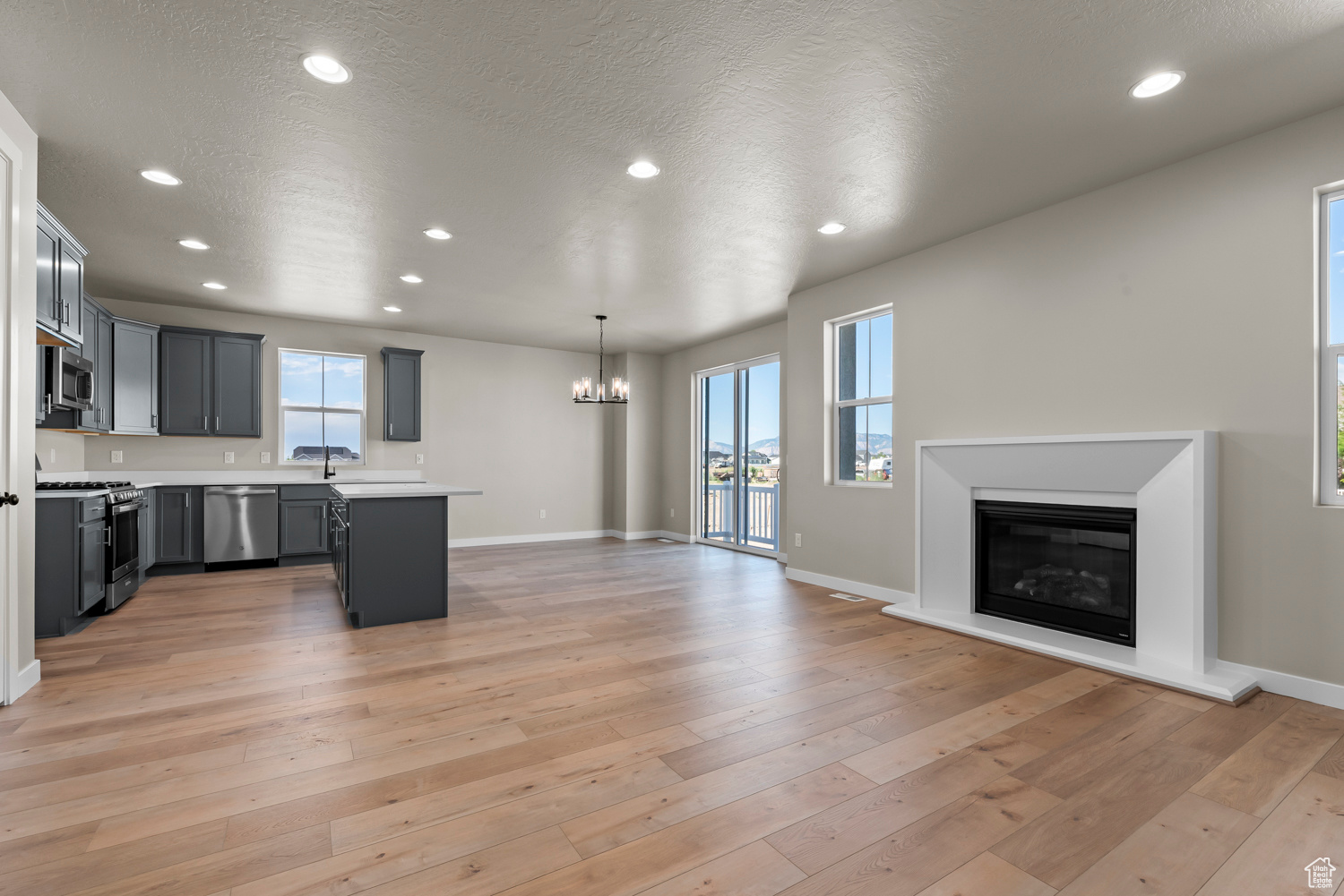 Unfurnished living room featuring light wood-type flooring, a notable chandelier, and a textured ceiling