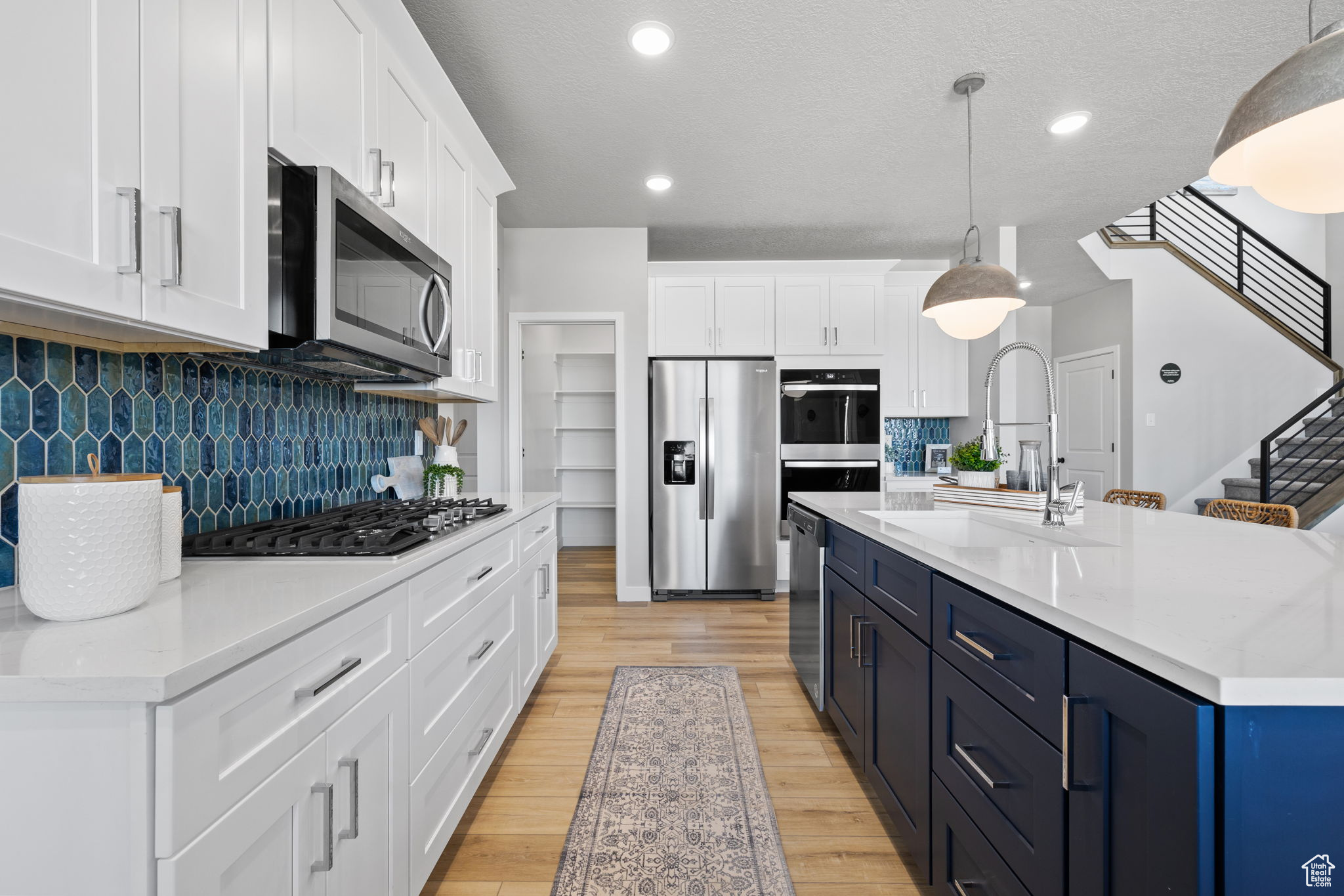 Kitchen featuring pendant lighting, white cabinets, backsplash, light hardwood / wood-style floors, and stainless steel appliances