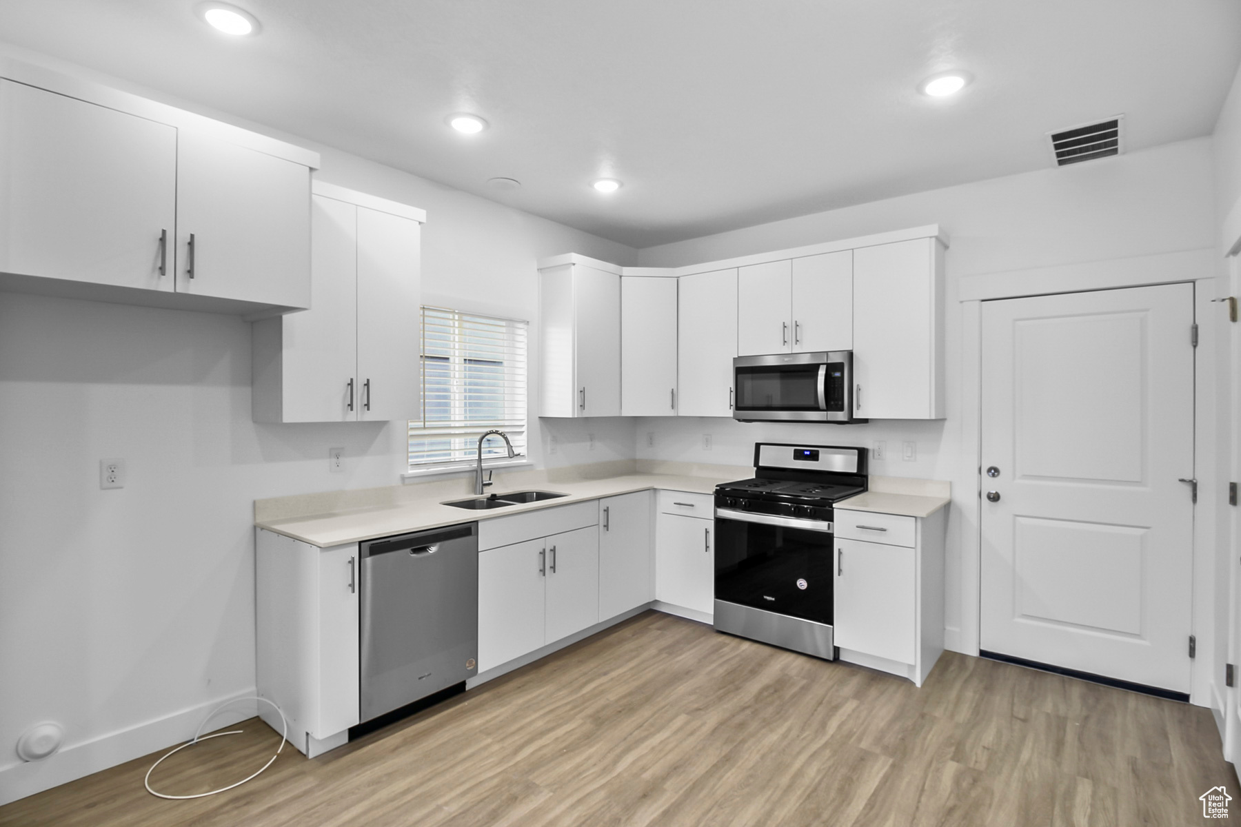 Kitchen with light hardwood / wood-style flooring, white cabinets, appliances with stainless steel finishes, and sink