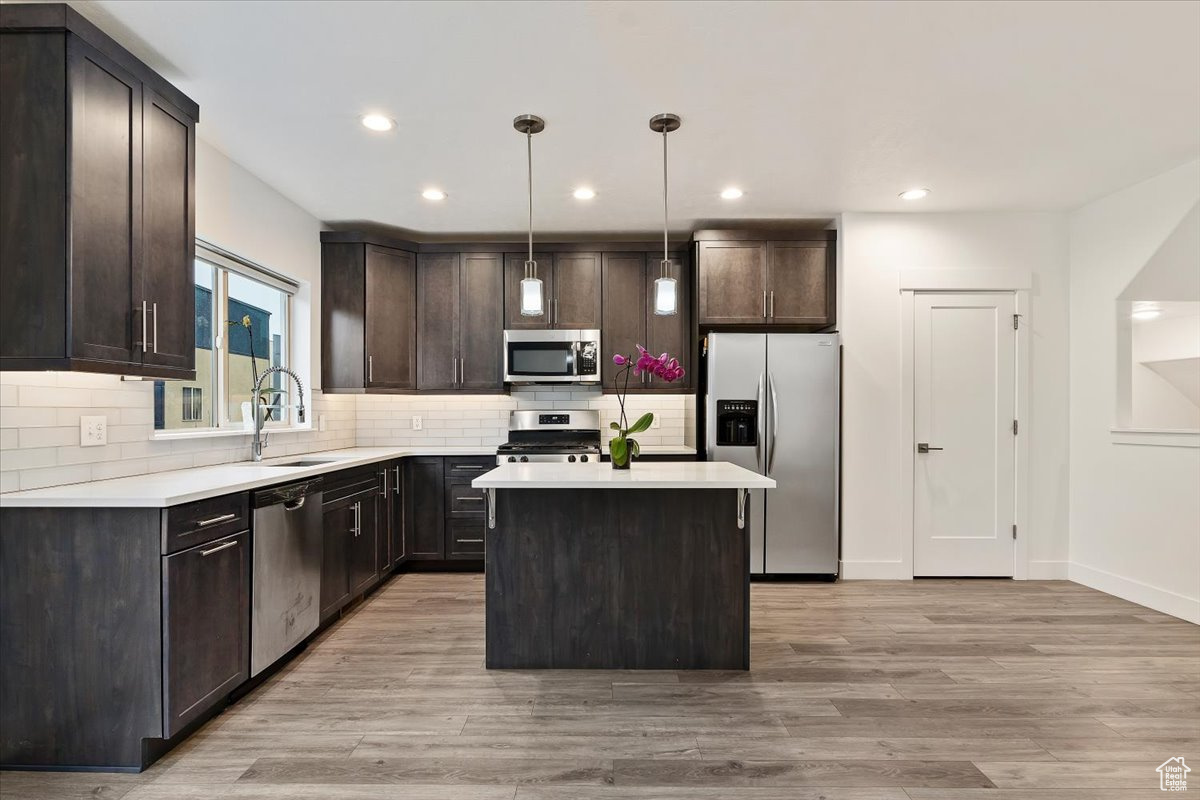 Kitchen featuring a kitchen island, dark brown cabinets, appliances with stainless steel finishes, backsplash, and light hardwood / wood-style floors