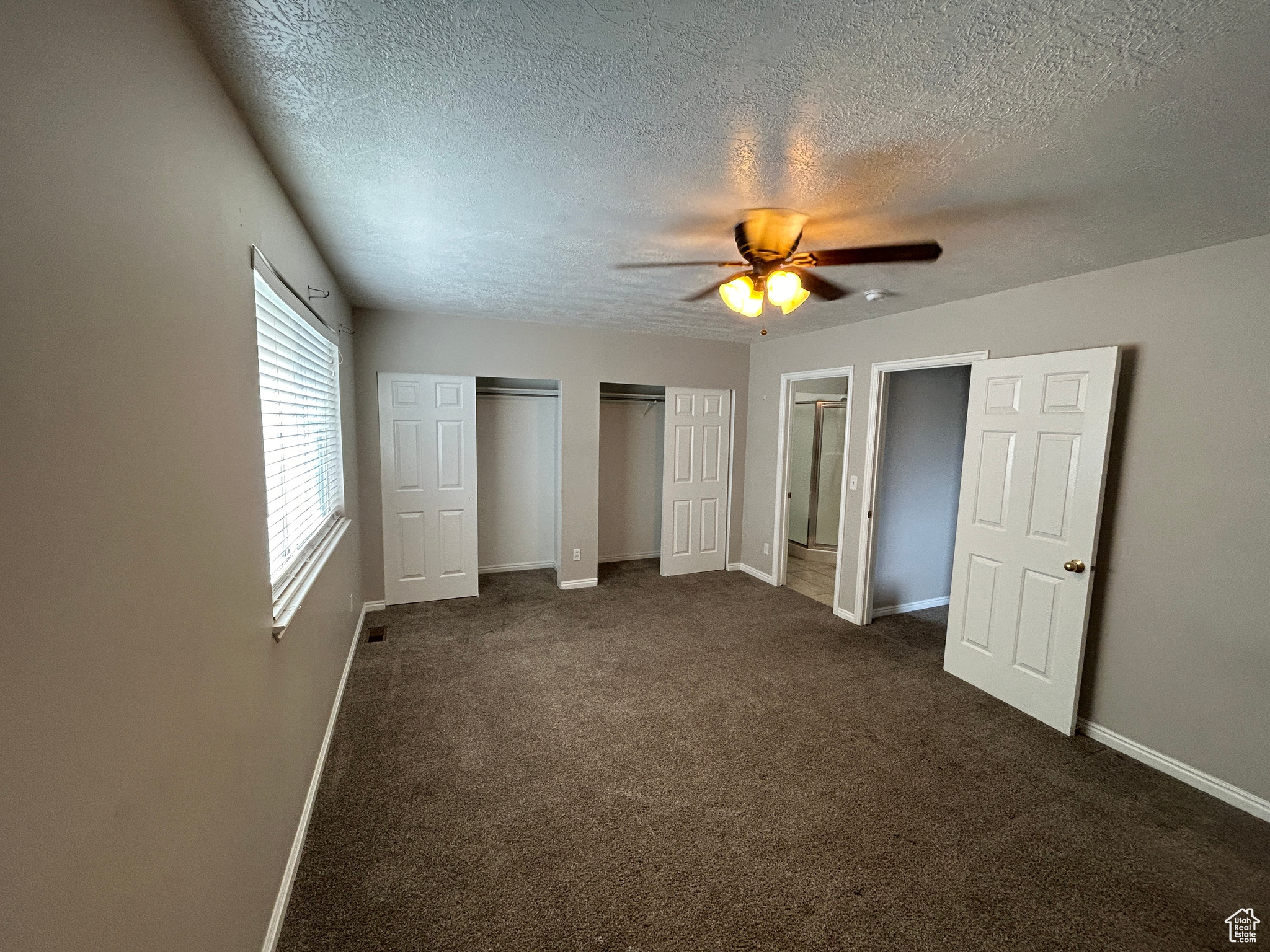Master bedroom 2 featuring dark carpet, two closets, ceiling fan, and a textured ceiling