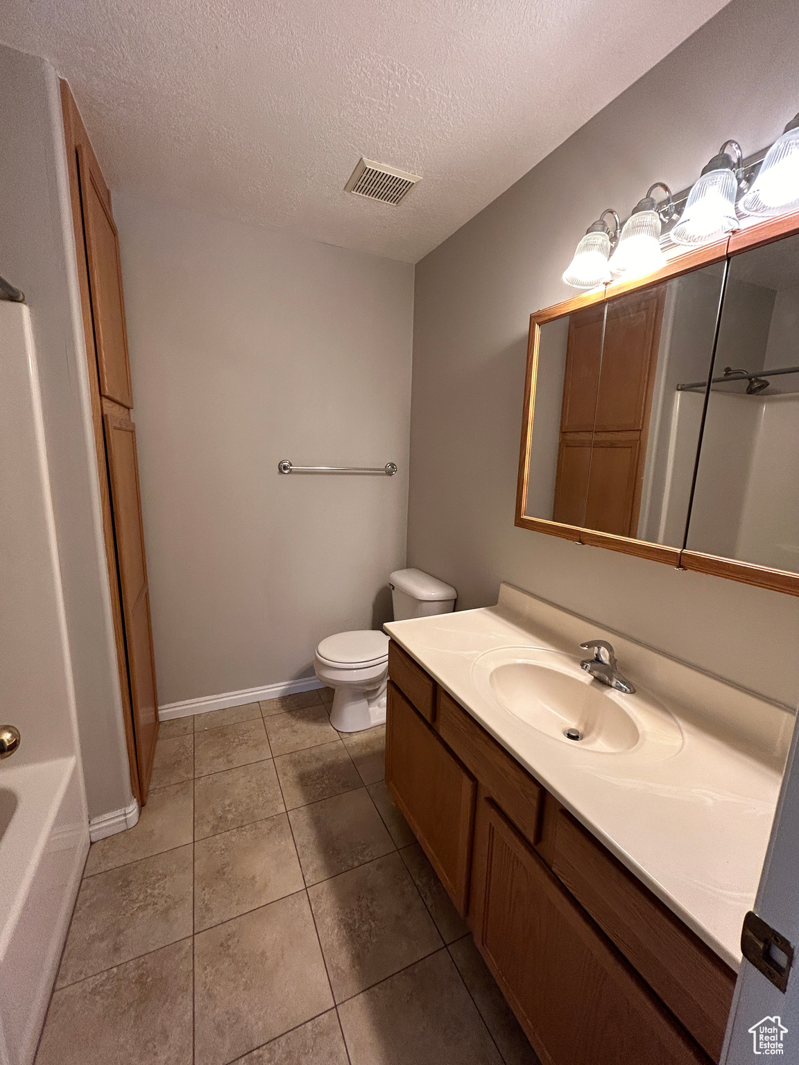 Full hall bathroom with toilet, tile floors, a textured ceiling, and vanity