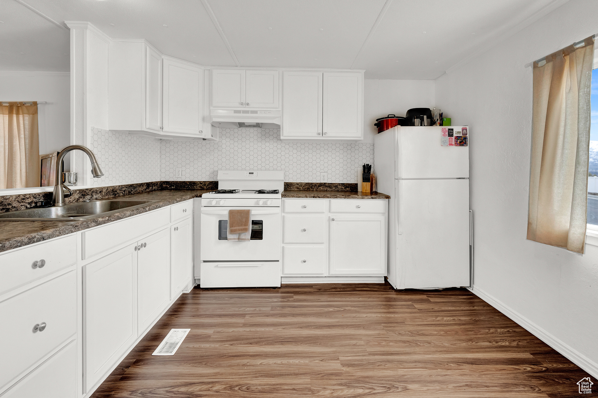 Kitchen with white cabinets, hardwood / wood-style floors, white appliances, and sink