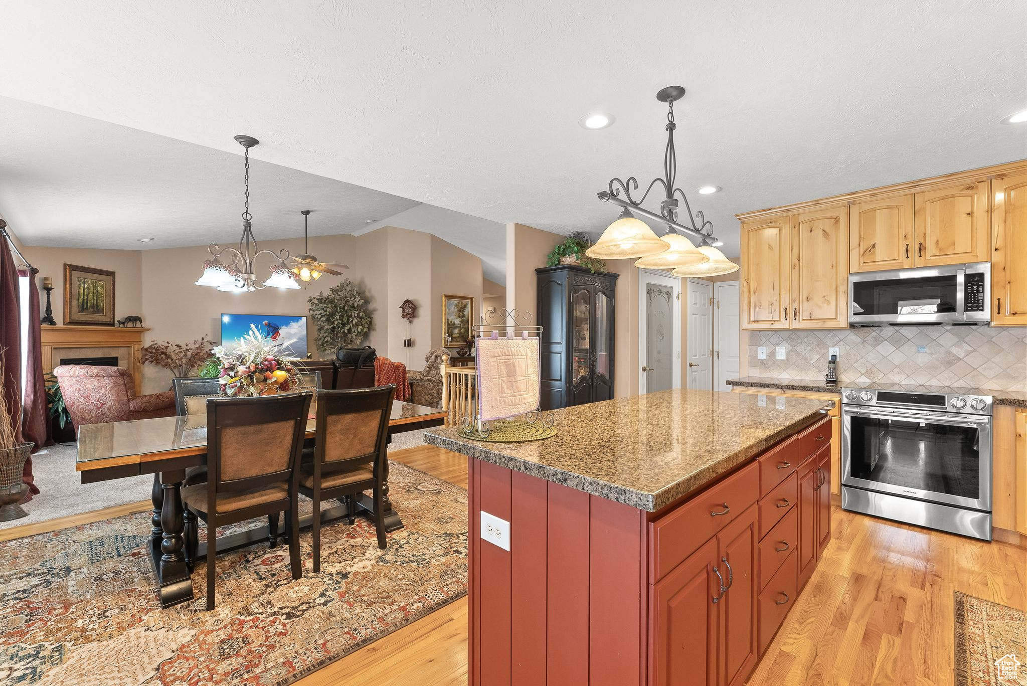 Kitchen with a notable chandelier, appliances with stainless steel finishes, light hardwood / wood-style floors, a kitchen island, and pendant lighting