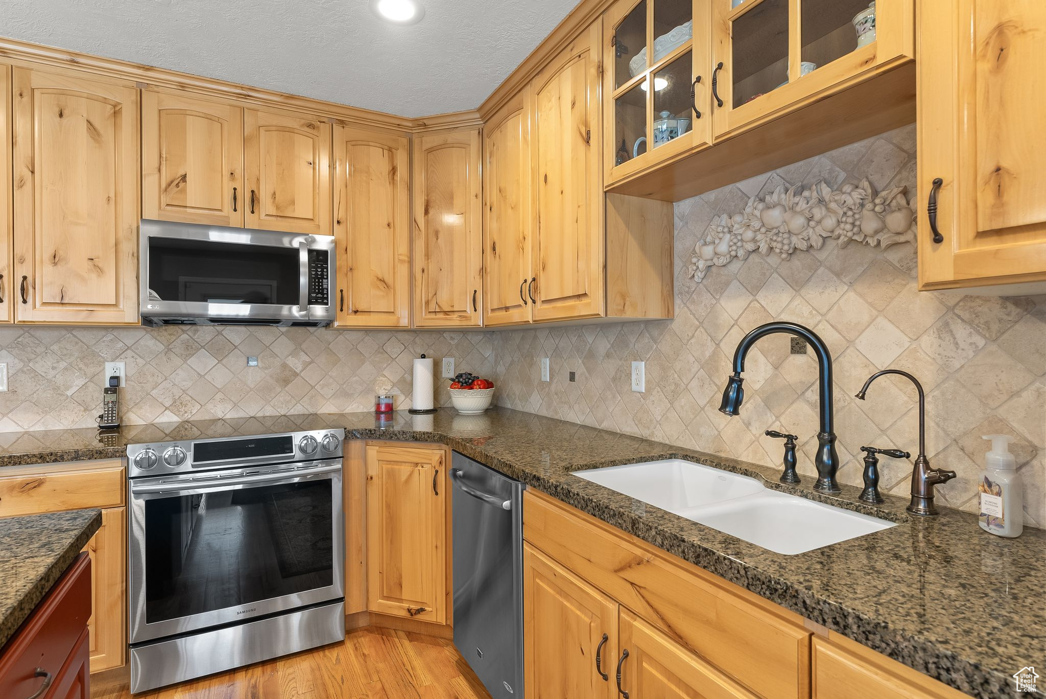 Kitchen featuring dark stone countertops, stainless steel appliances, light wood-type flooring, backsplash, and sink