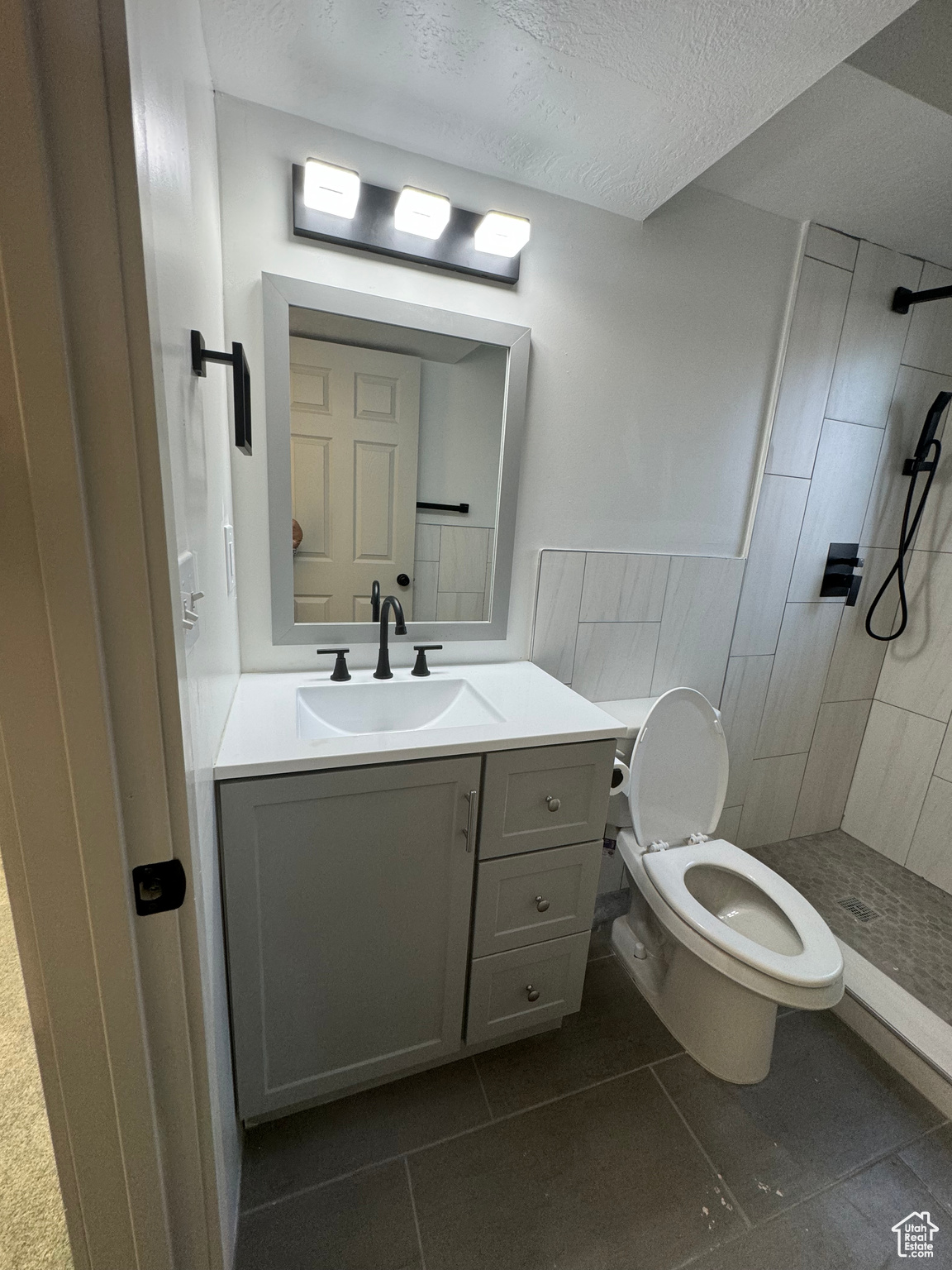 Bathroom with a tile shower, tile floors, vanity with extensive cabinet space, and toilet