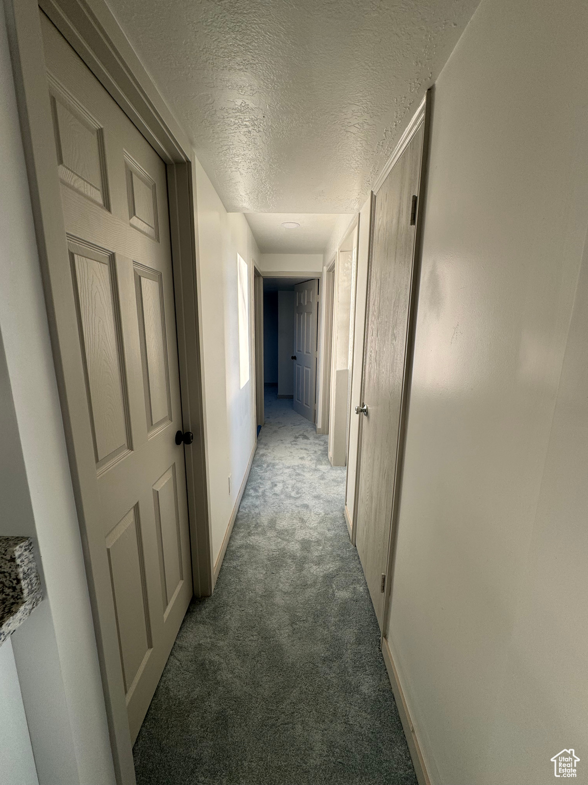 Corridor featuring a textured ceiling and dark carpet