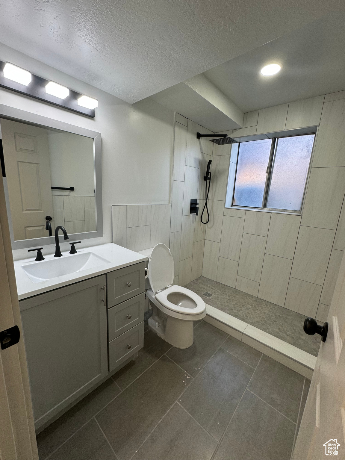 Bathroom with toilet, a textured ceiling, vanity, tile floors, and a tile shower