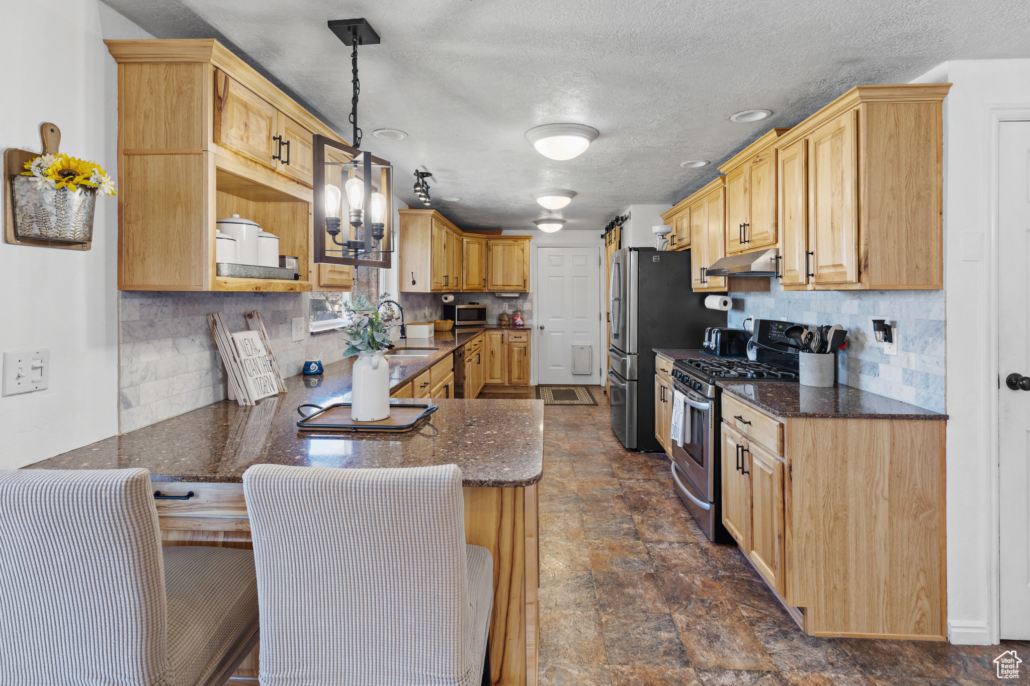 Kitchen with pendant lighting, dark tile floors, appliances with stainless steel finishes, and backsplash